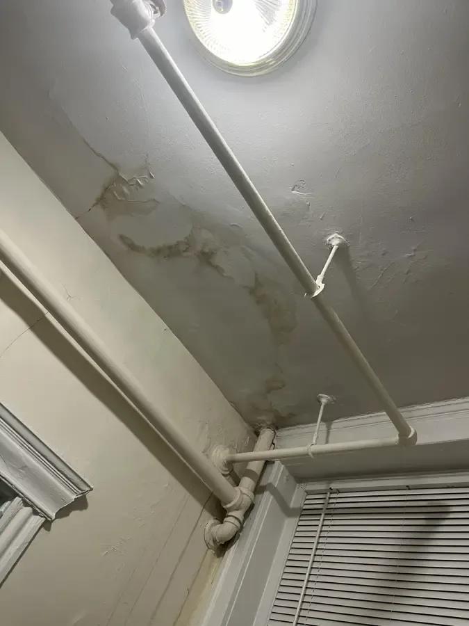 Water stains running across a ceiling beside an old heating pipe