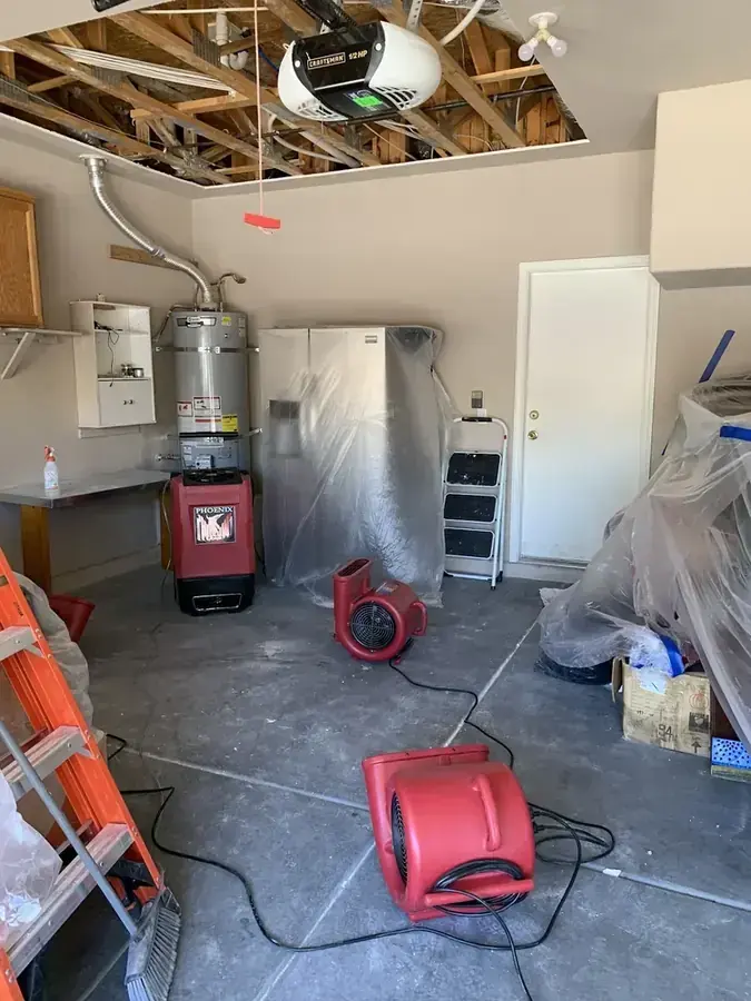 Air movers and a dehumidifier drying a garage with the ceiling opened after a water heater leak