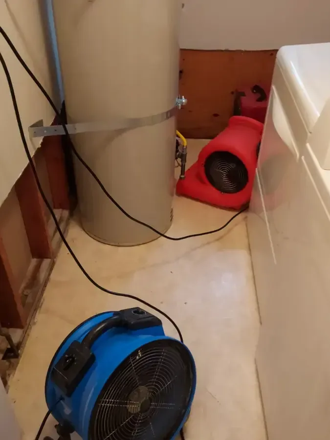 Blue and red air movers drying the floor beside a washing machine