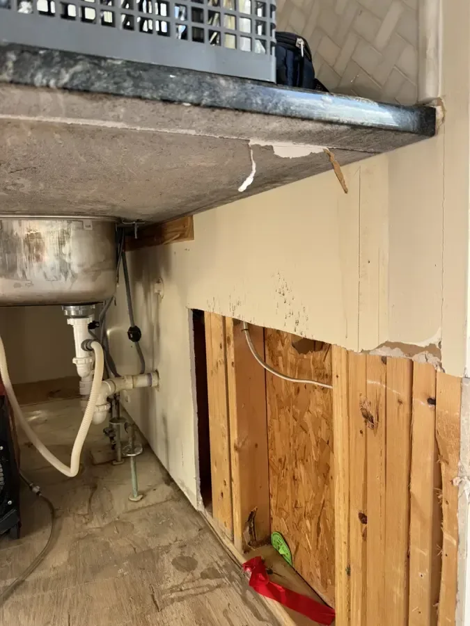 Sink cabinet and wall opened to expose damp framing